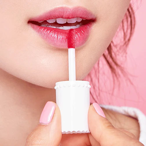 Person applying a white lip balm to their lips with a pink background