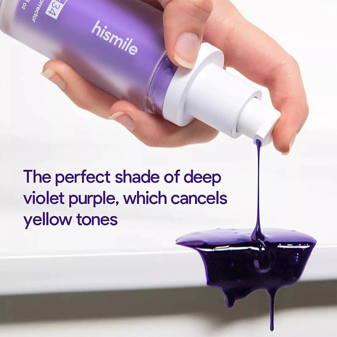 Hand holding a 'hismile' bottle with purple liquid being poured onto a white surface.